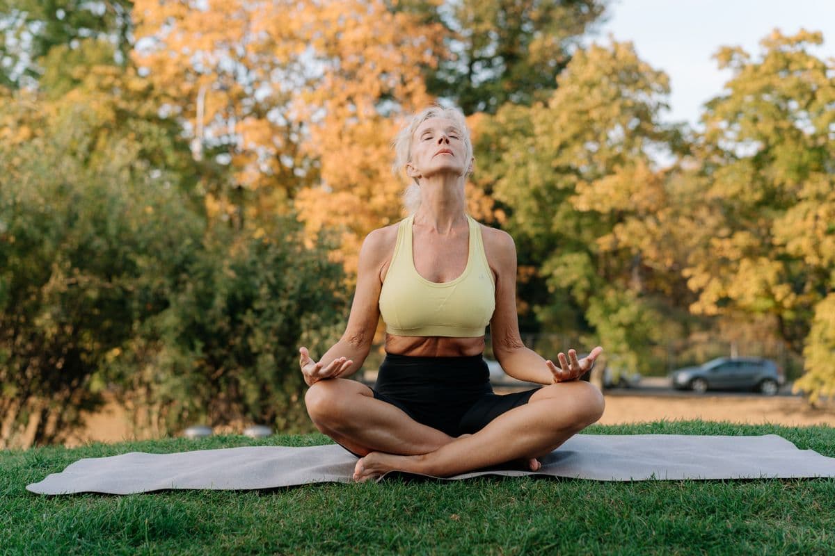 A woman meditating outdoors in a sunlit park